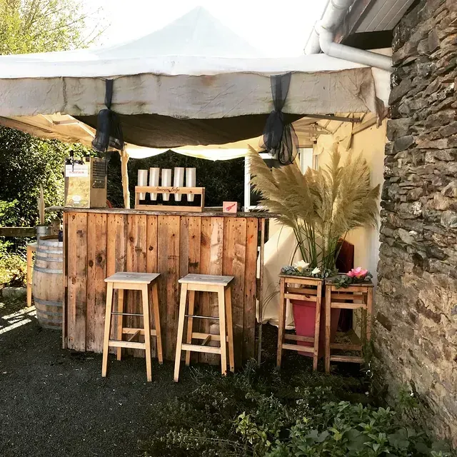 Un bar extérieur en bois sous une tente blanche, avec deux tabourets.