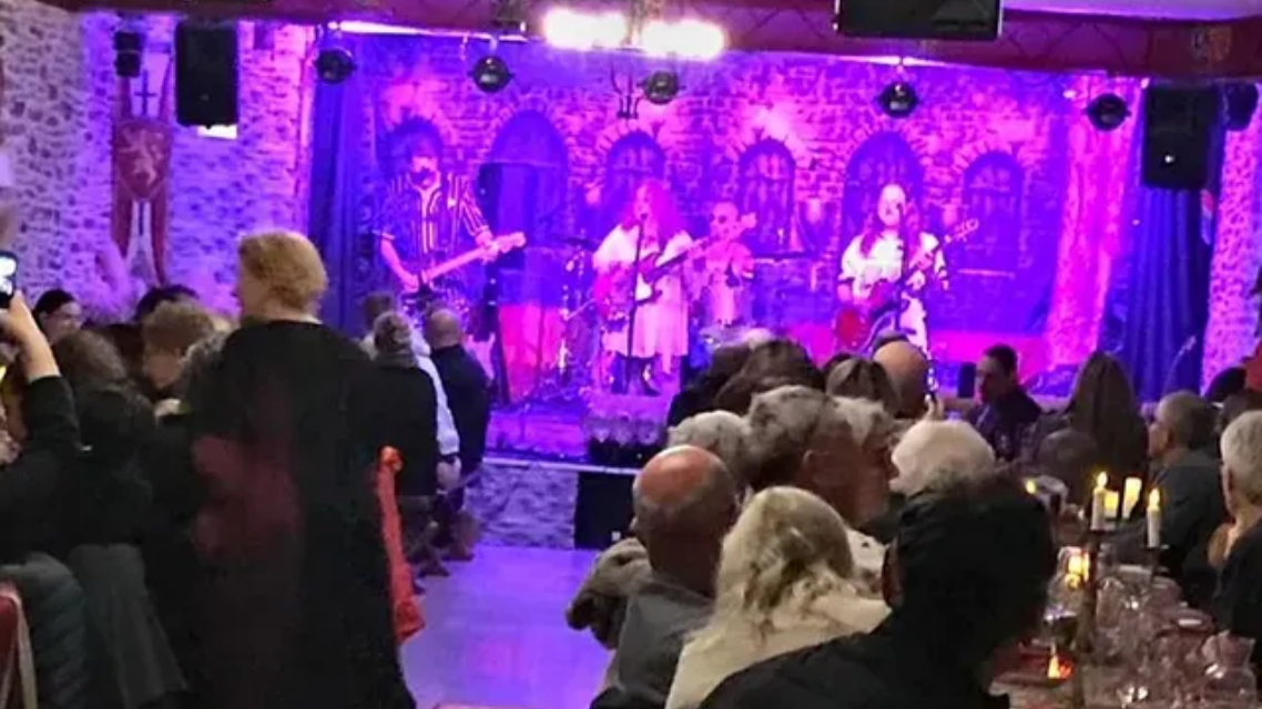 Un groupe se produit sur une scène baignée d'une vive lumière violette devant un public assis.