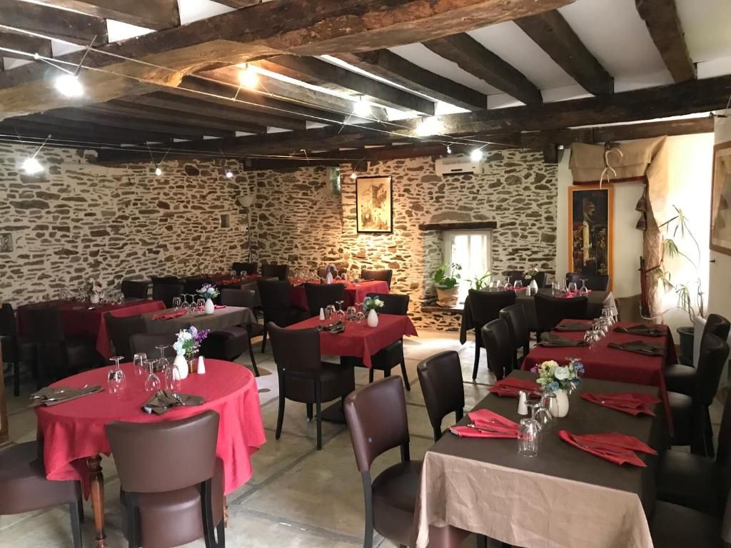 Une salle à manger rustique avec des murs en pierre, des poutres apparentes au plafond et des tables recouvertes de nappes rouges et neutres.