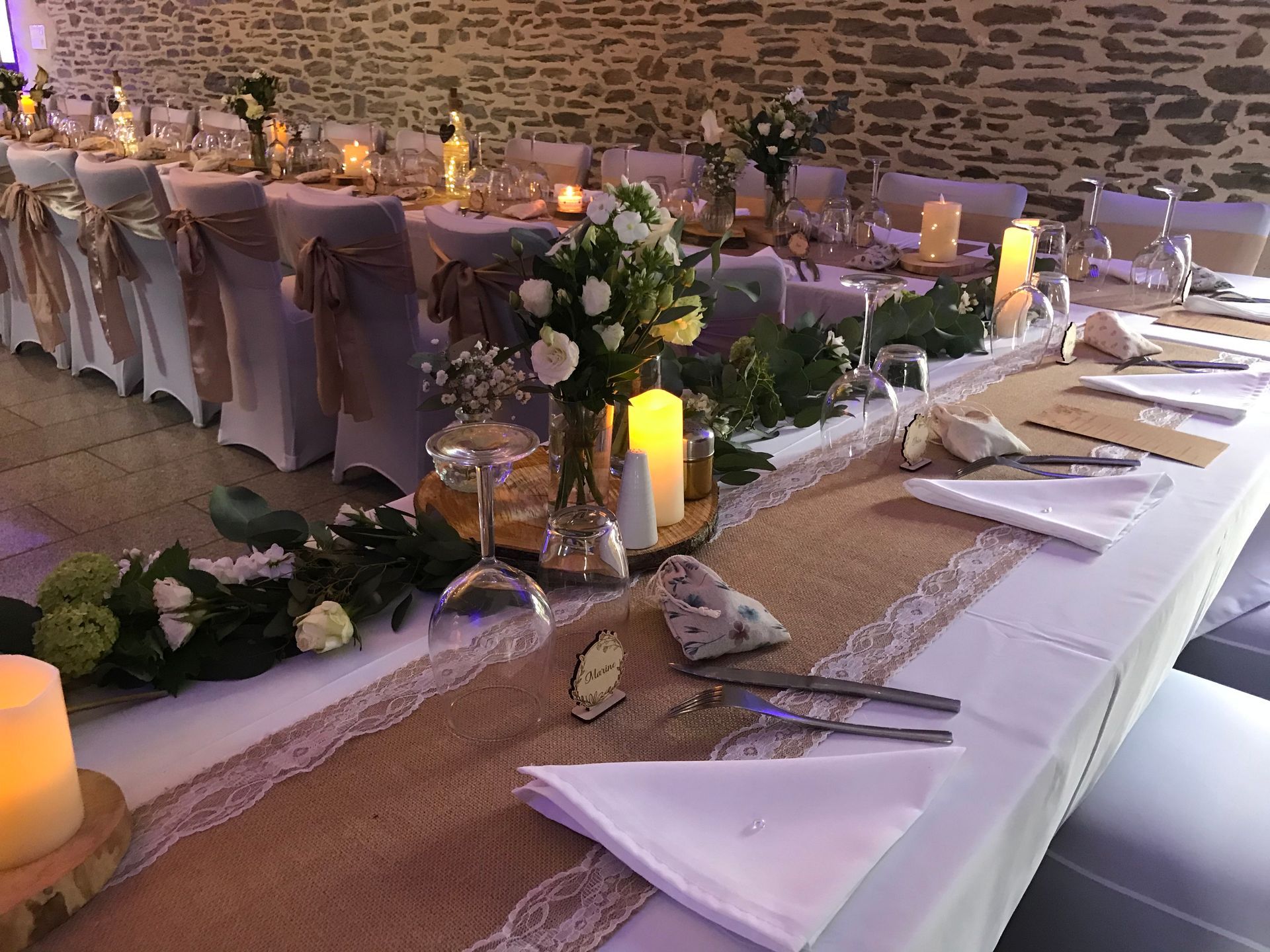 Une longue salle aménagée pour un événement formel, avec des tables nappées de blanc, des chaises rouges et des murs en pierre ornés d'une tapisserie.