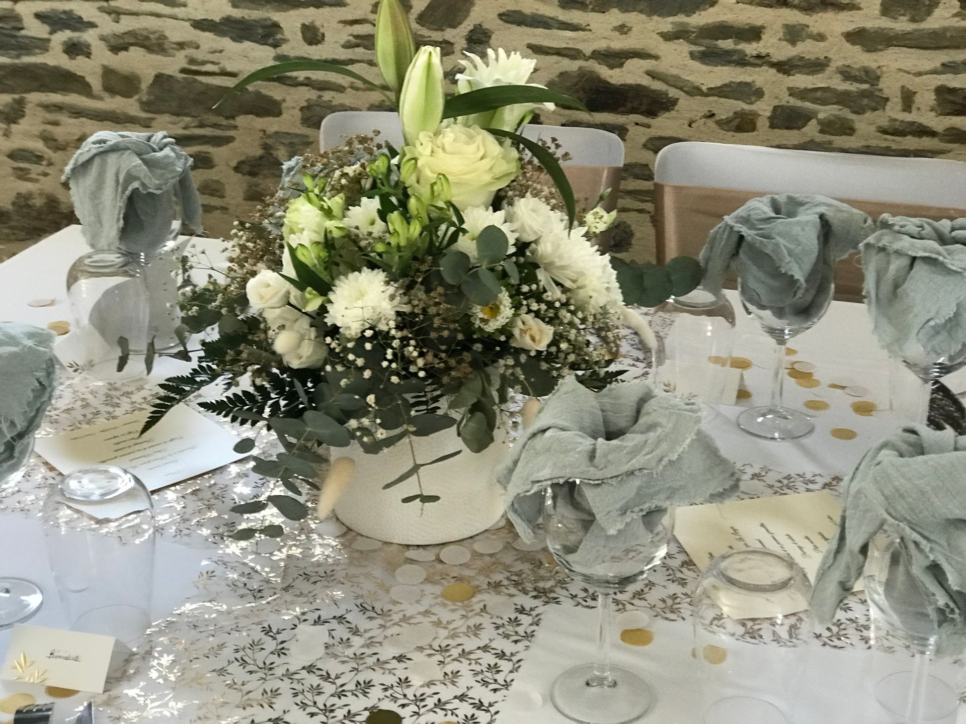Centre de table floral sur une table de banquet décorée avec des nappes blanches, de la verrerie et des serviettes grises pliées.