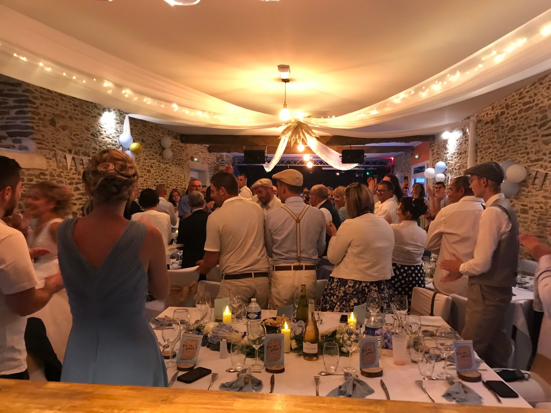 Un groupe de personnes se réunit dans un lieu rustique aux murs de pierre, debout autour de tables à manger lors d'un événement social.