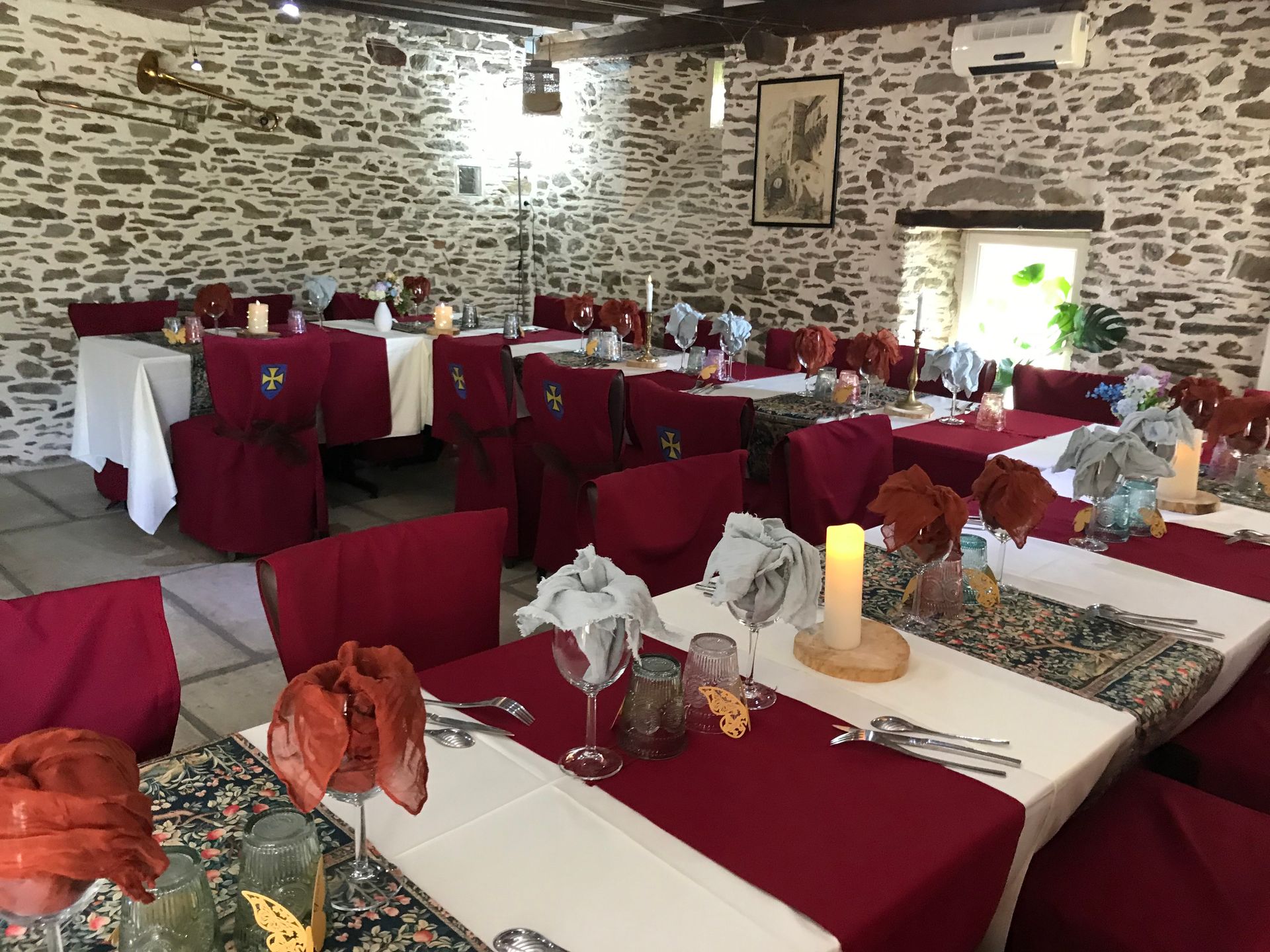 Une table de mariage ronde avec nappes blanches, chemins de table en toile de jute, un centre de table floral, des couverts et des chaises.