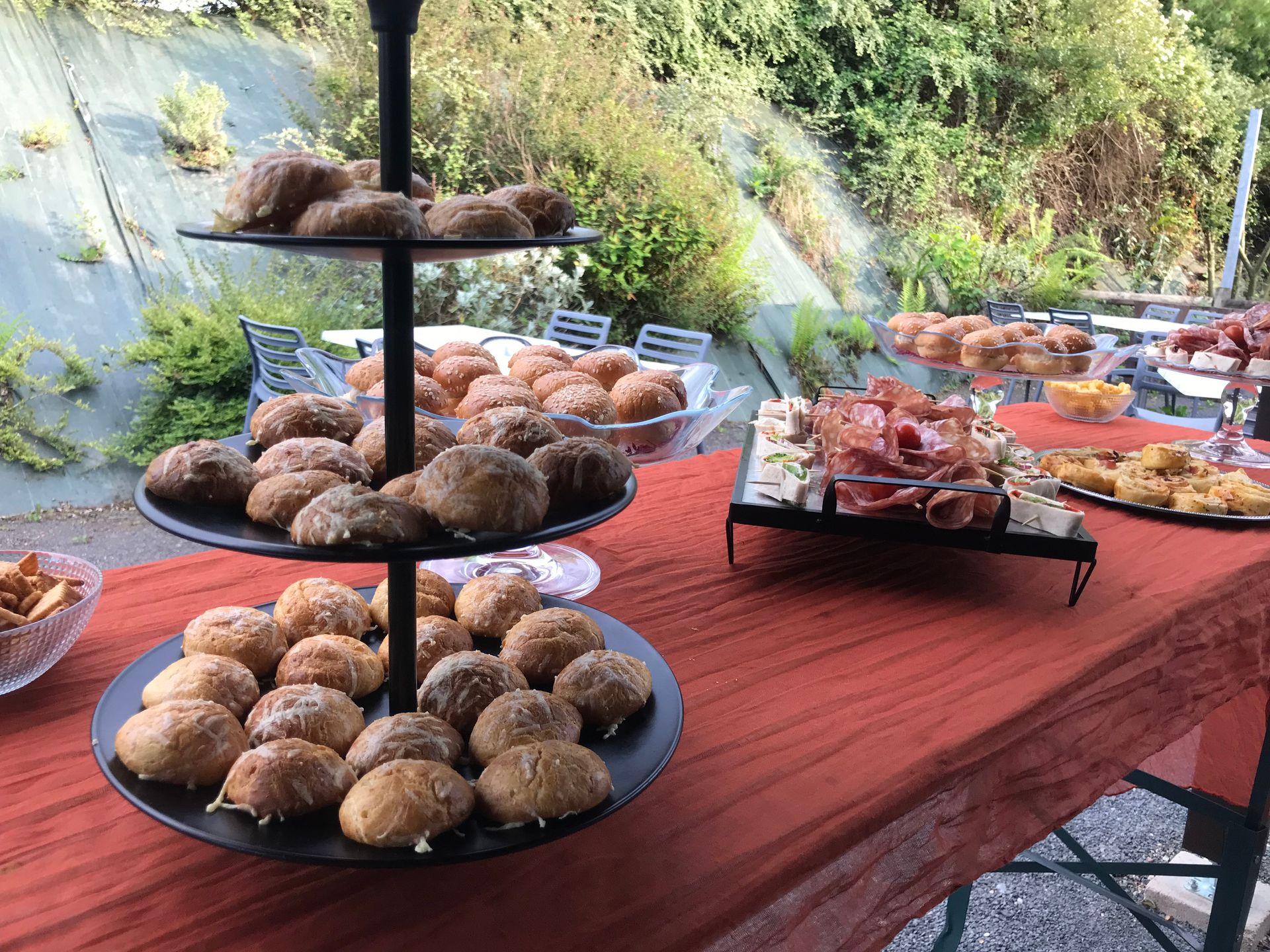 Un buffet sur une nappe orange, présentant un présentoir à trois étages de petits pains et d'amuse-gueules assortis, en extérieur.