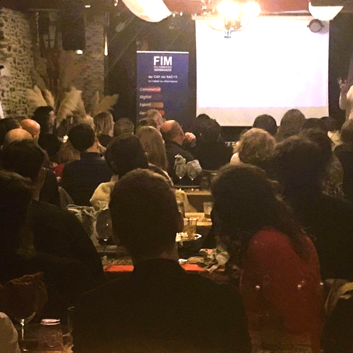 Un espace événementiel bondé, avec des murs en pierre rustiques, des guirlandes lumineuses et un bar en bois au premier plan, avec des plateaux vides.
