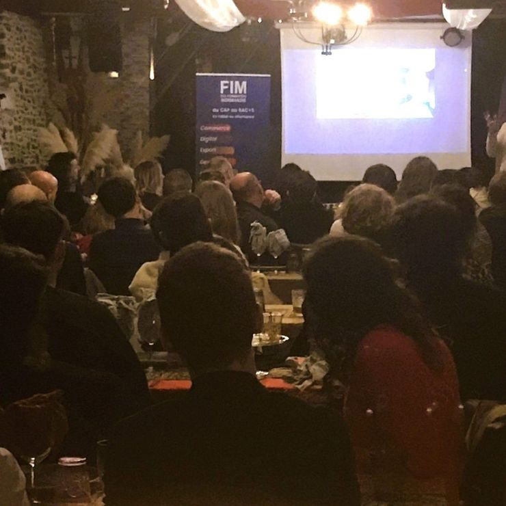 Un groupe de personnes assises dans une pièce rustique et sombre regardent une présentation projetée sur un écran.
