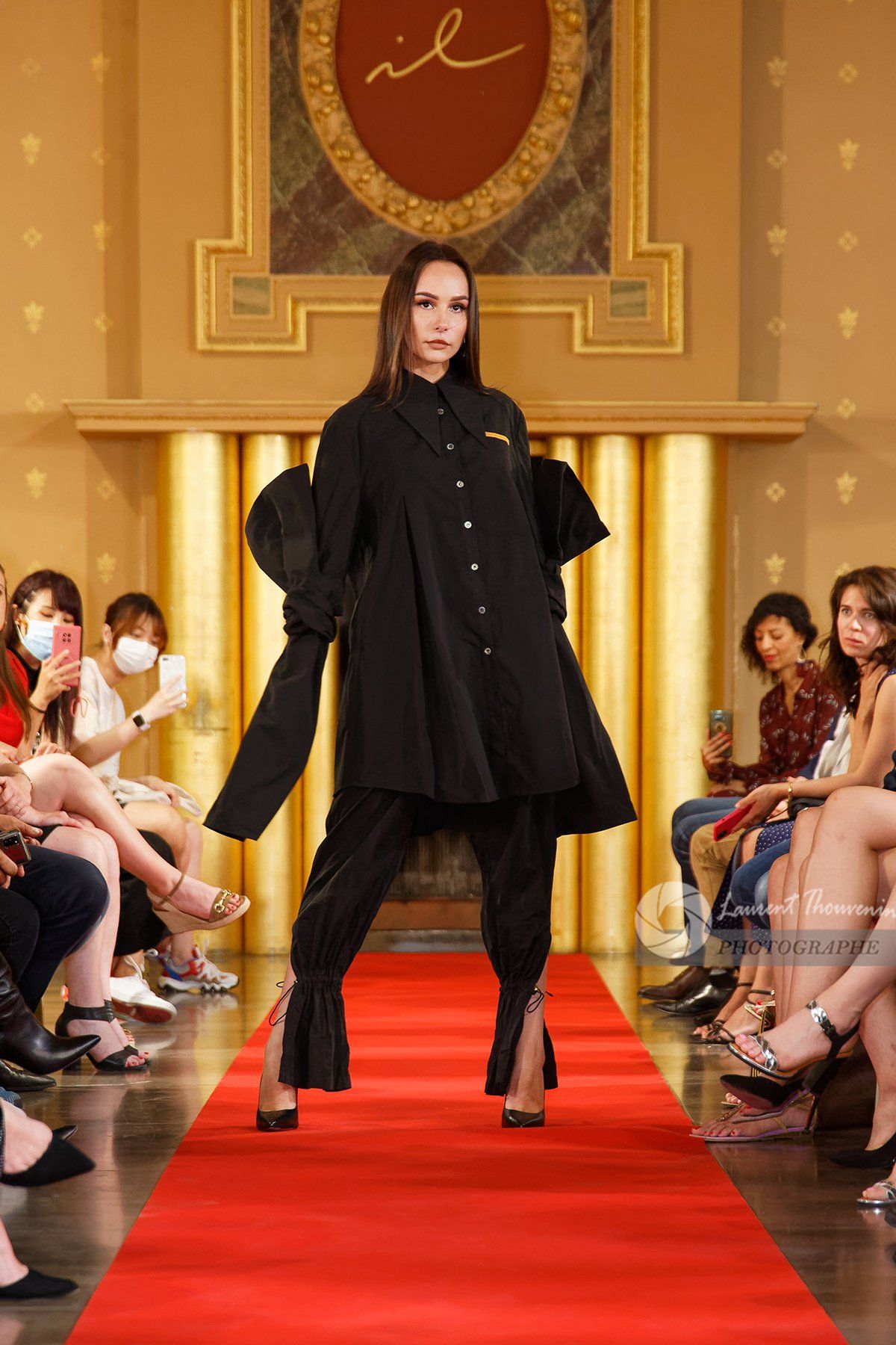 Mannequin en tenue noire sur un podium ; décor d'un défilé de mode.