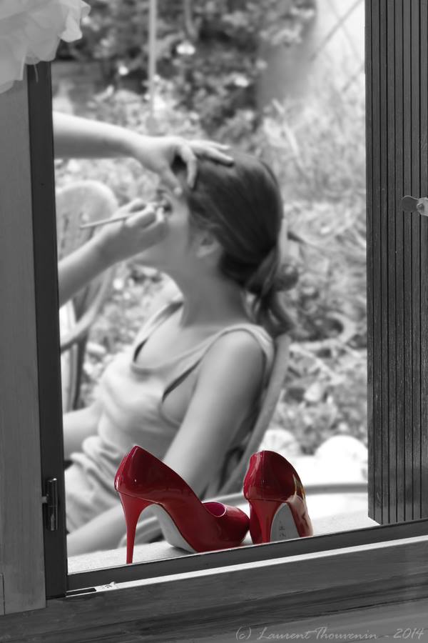 Talons hauts rouges sur le rebord de la fenêtre ; une personne se fait maquiller. Couleur sélective.