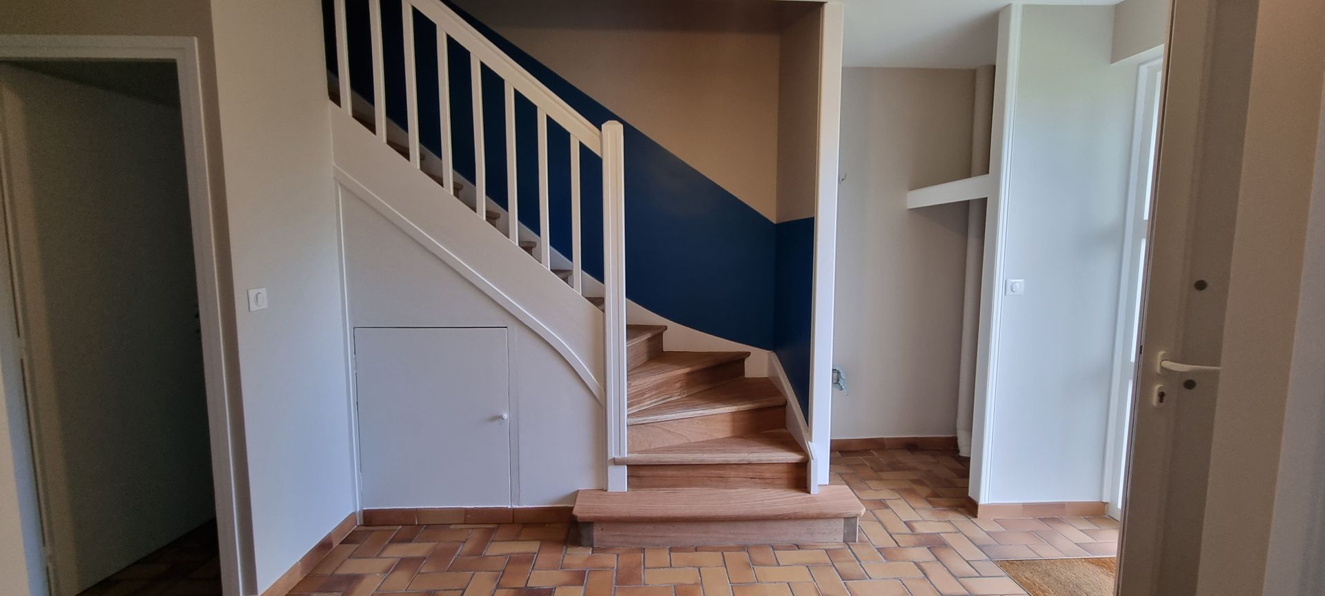 Escalier avec rampe blanche et mur d'accent bleu marine ; marches et sol en bois.