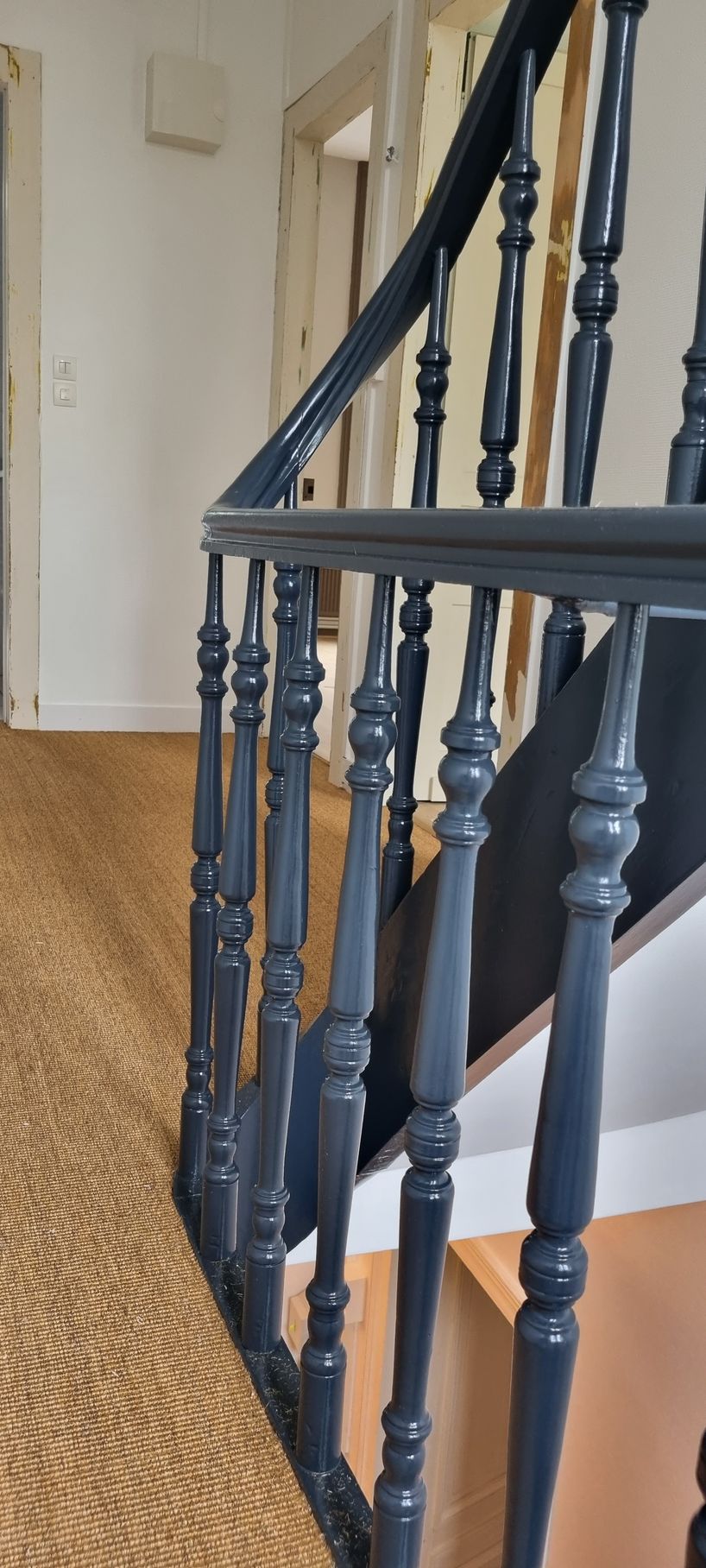 Escalier en bois avec rampe bleu foncé et balustres décoratifs, revêtement de sol en fibres naturelles.