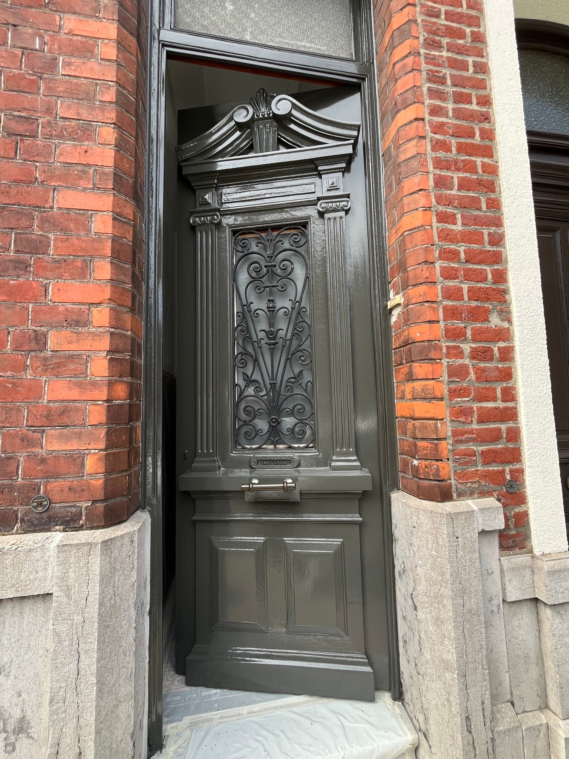 Porte grise ornée de ferronneries dans un bâtiment en briques rouges.