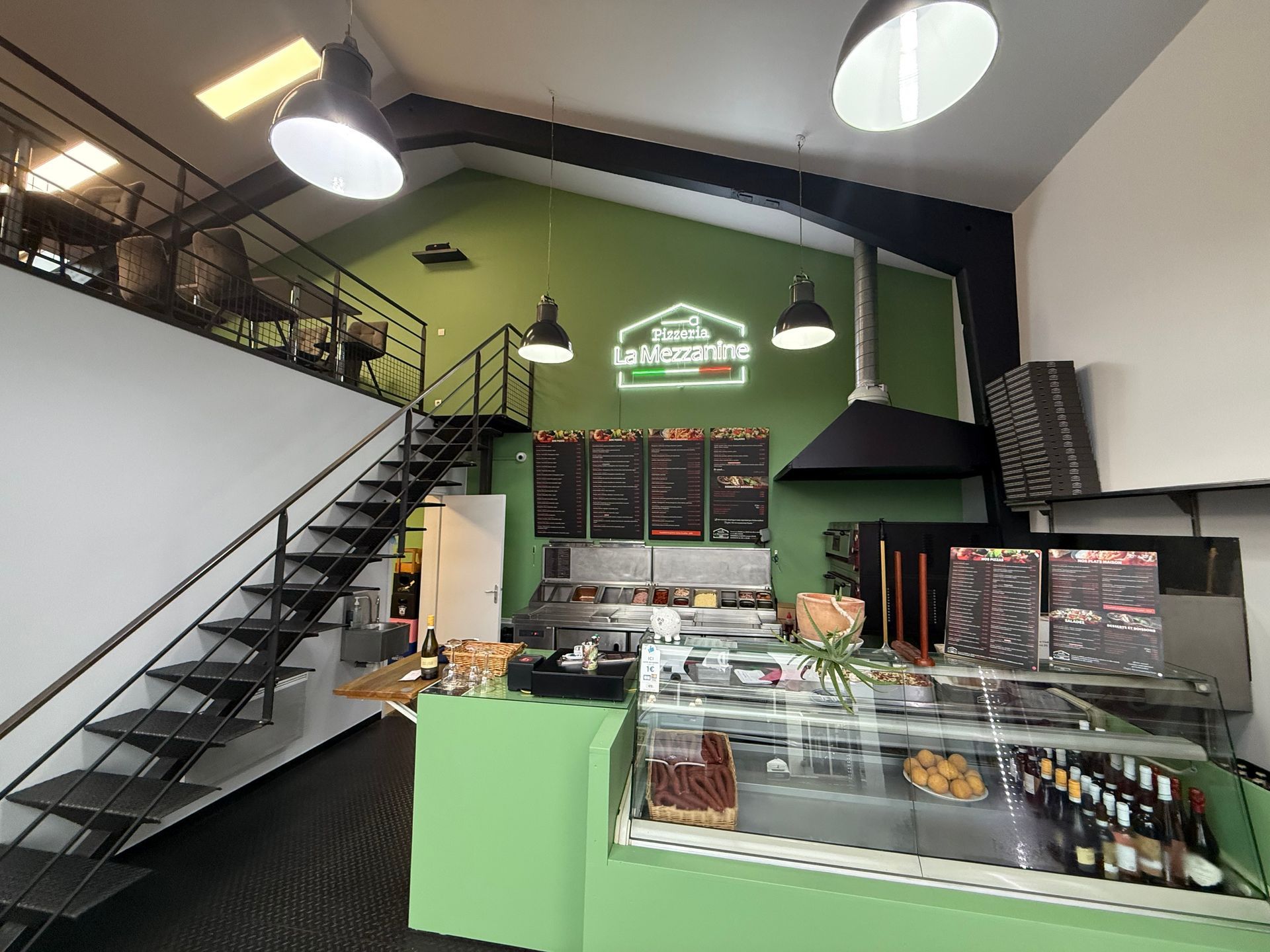 Intérieur d'un restaurant avec des murs verts, un escalier noir et des vitrines présentant des aliments.