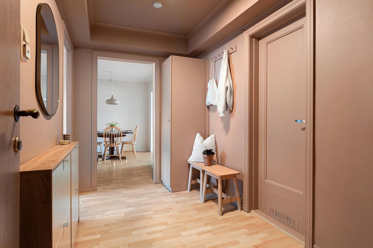 Un couloir peint en rose, avec un parquet clair, mène à une salle à manger. On y trouve un banc en bois et un miroir.