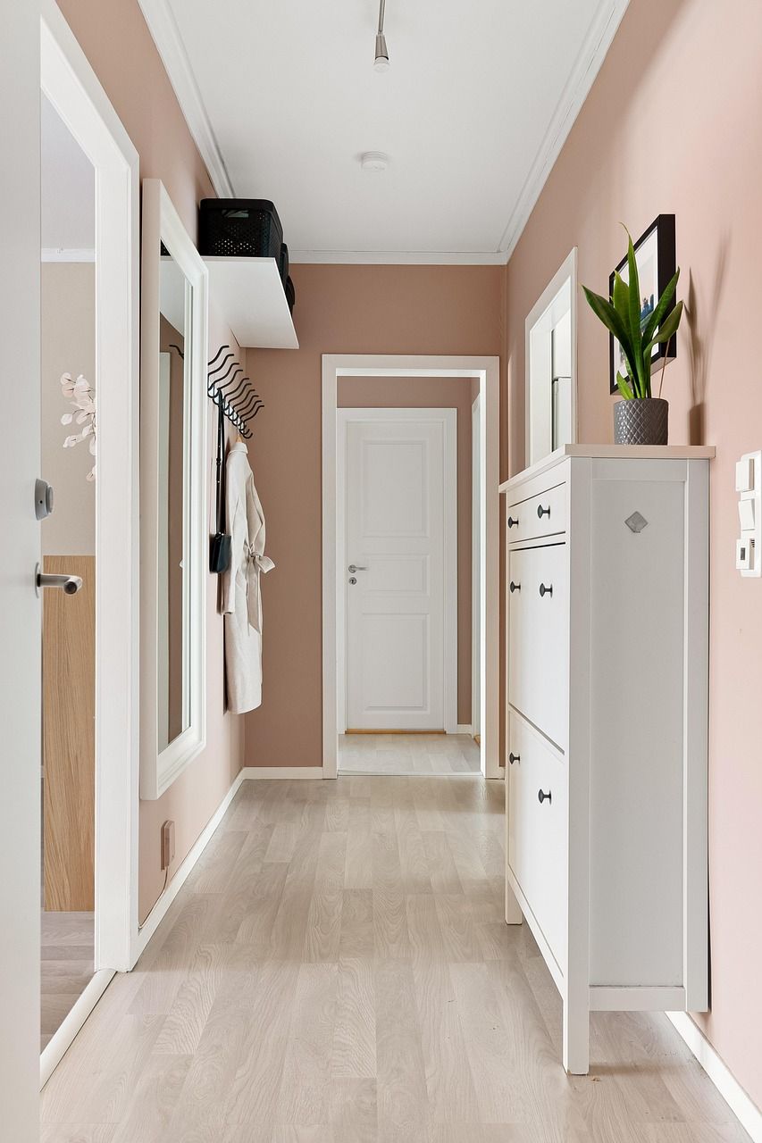 Long couloir aux murs rose pâle, aux moulures blanches et doté d'un meuble à chaussures blanc.