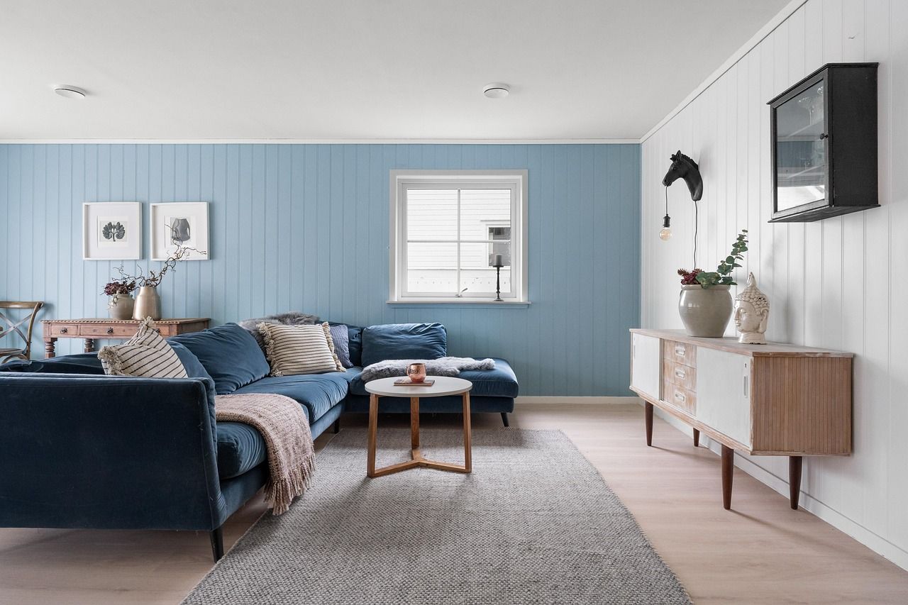 Salon aux murs bleus avec un canapé d'angle bleu marine, un parquet clair et un meuble blanc et bois.