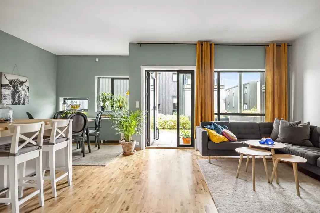 Espace de vie ouvert avec parquet, canapé gris et table donnant sur une terrasse.