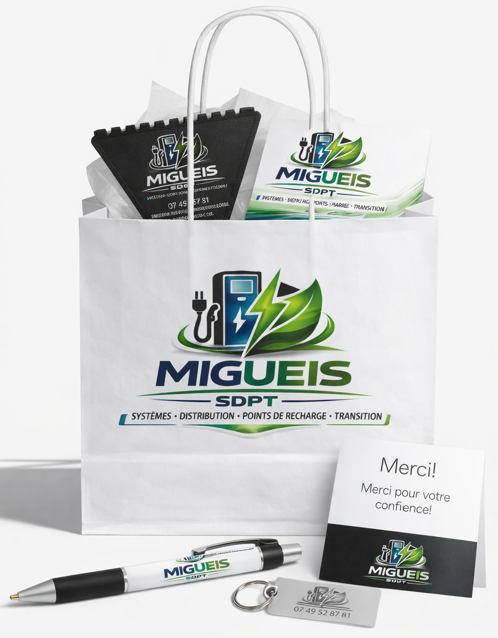 Un sac cadeau en papier blanc orné du logo MMIGUEIS.SDPT, accompagné d'un stylo, d'un porte-clés et d'une carte de remerciement.