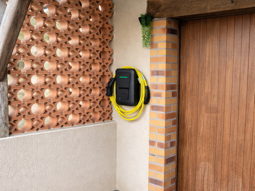 Câble jaune enroulé sur le mur à côté d'un pilier en briques et d'une porte en bois dans la terrasse extérieure.