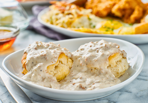 Plated biscuits and gravy with breakfast food in the background