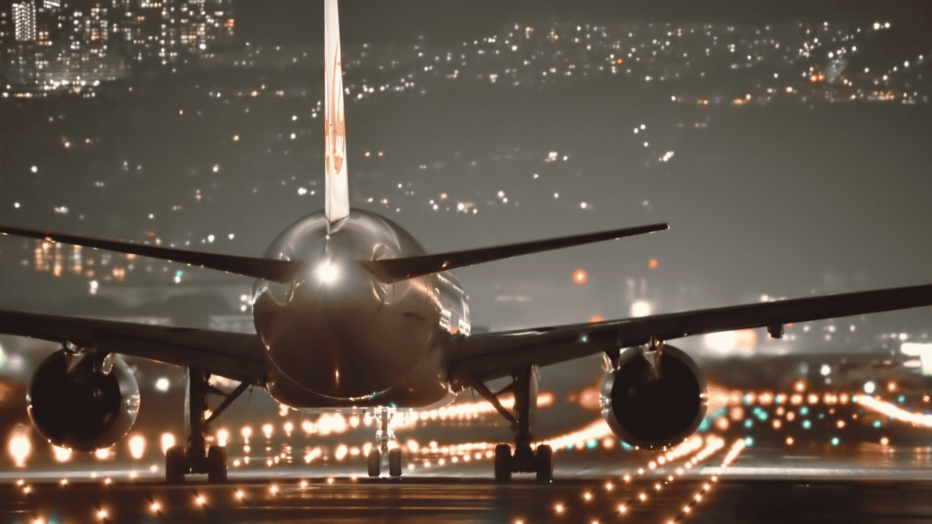 Rear angled view of airplane on runway at night with city lights in the distance