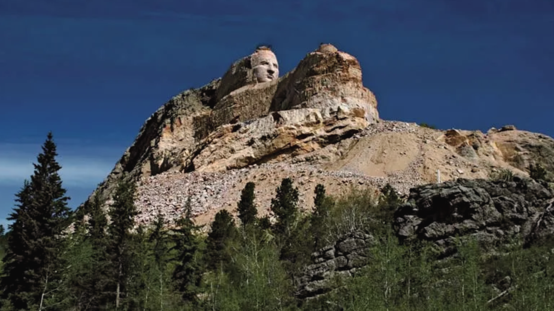 Clear view of Crazy Horse Memorial on a clear sunny day with lush pine trees