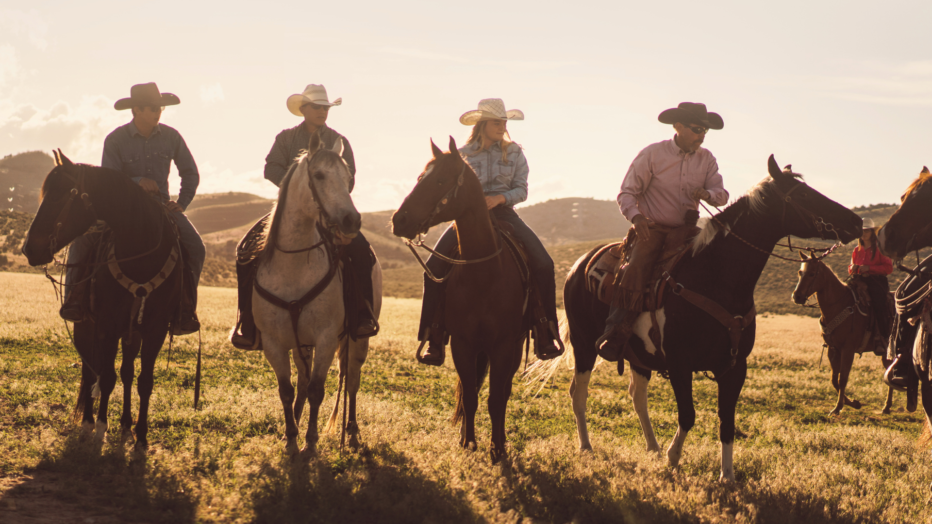 Men in cowboy hats riding horses in grassy field