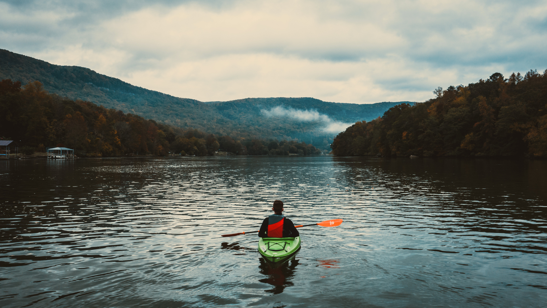 A man kayaking outdoors in calm water with surrounding trees