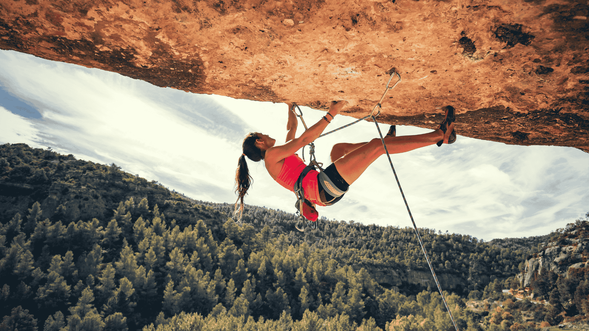 Woman performing extreme horizontal rock climbing with pine trees nearby