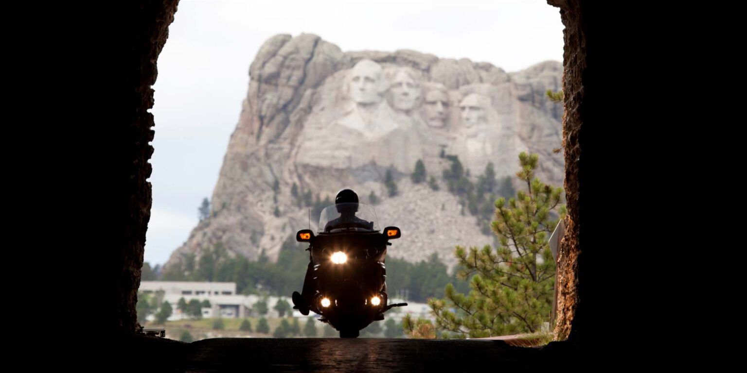 Person driving a motorcycle through a tunnel with Mount Rushmore in the distance