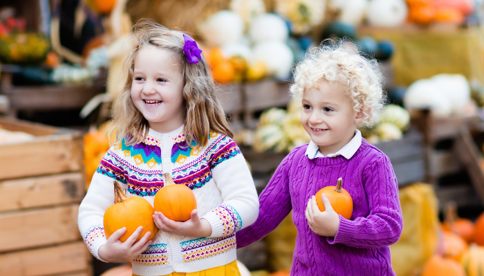 happy children in a pumpkin patch holding small pumpkins 