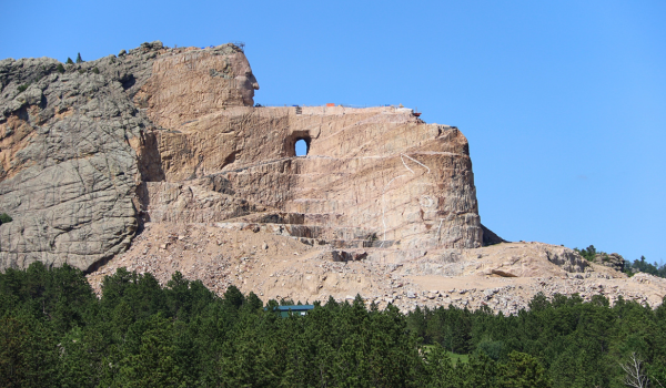 Side profile of Crazy Horse Memorial on a sunny day with lush green pine trees