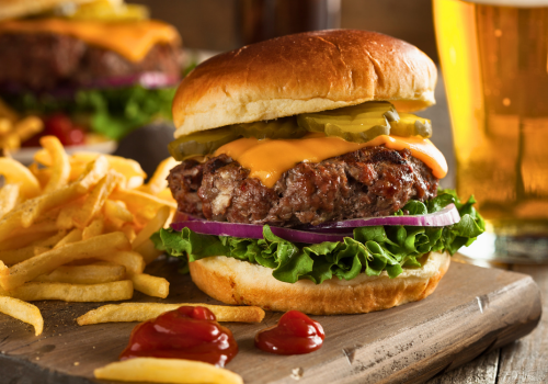 Large, stacked burger with fries and ketchup on the side, and beer in background