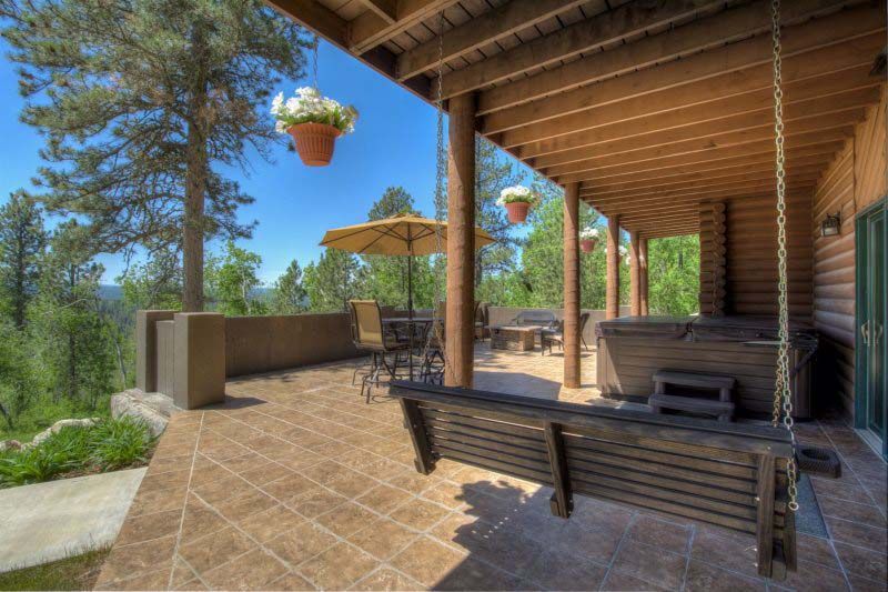Covered porch with swing, hot tub, and hanging flower baskets, overlooking the woods on a sunny, clear day