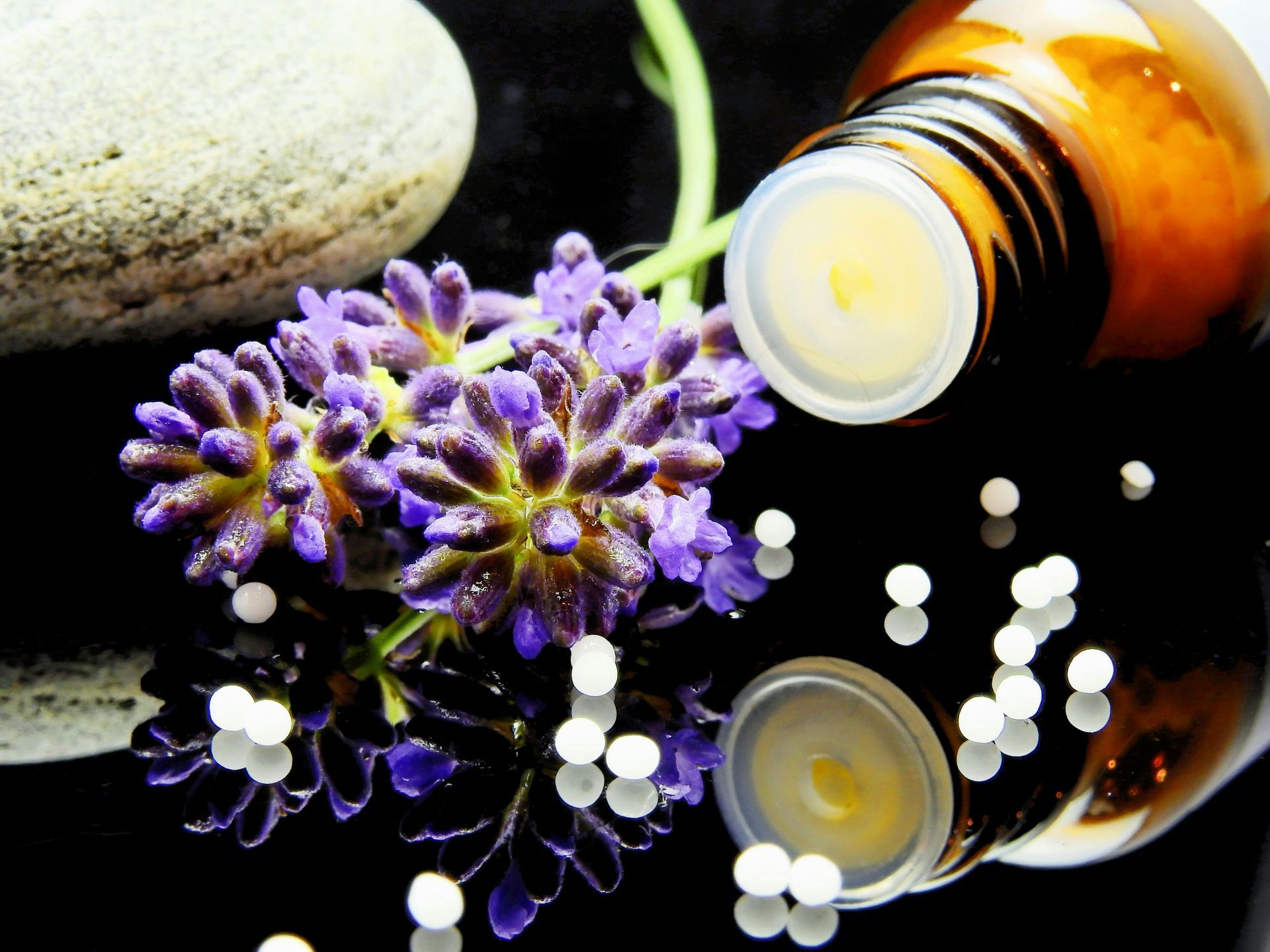 Brown fragrance bottle with lavender and a stone on a reflective spa surface