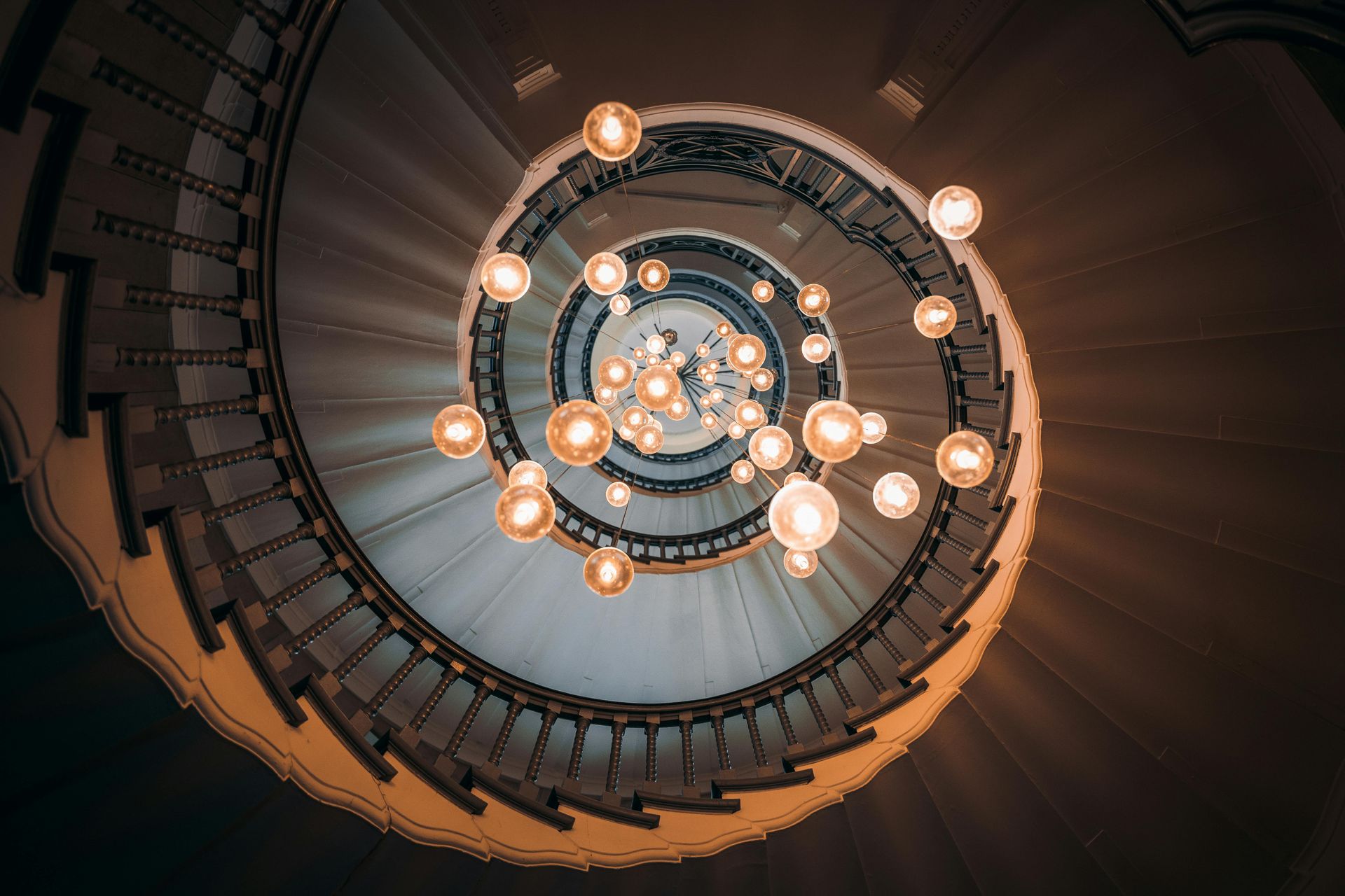 Large spiral stair case of an old museum looking up at a chandelier