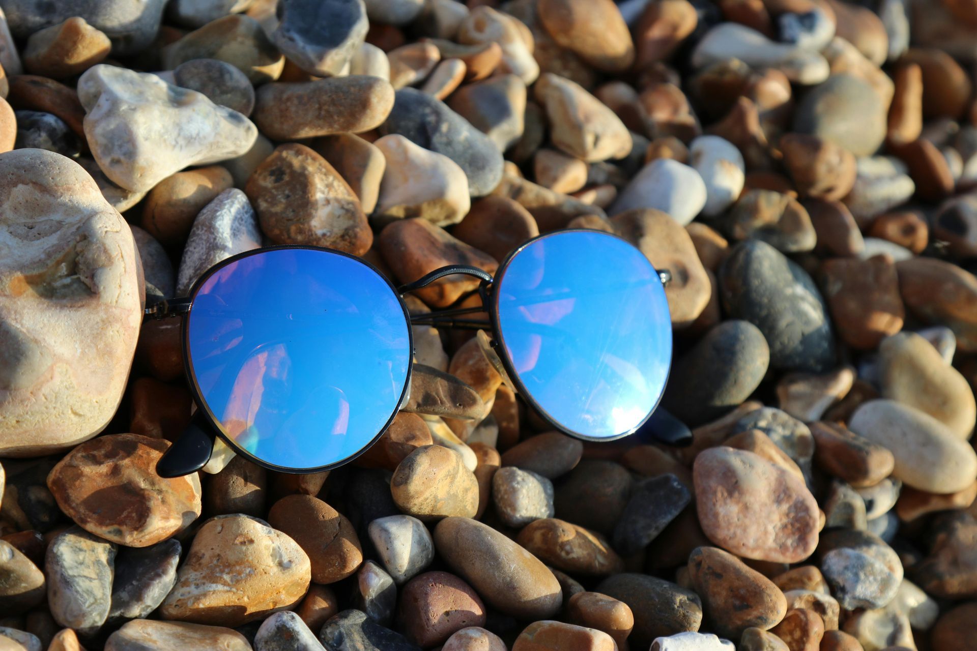 Blue reflection sunglasses sitting in shoreline of pebbles
