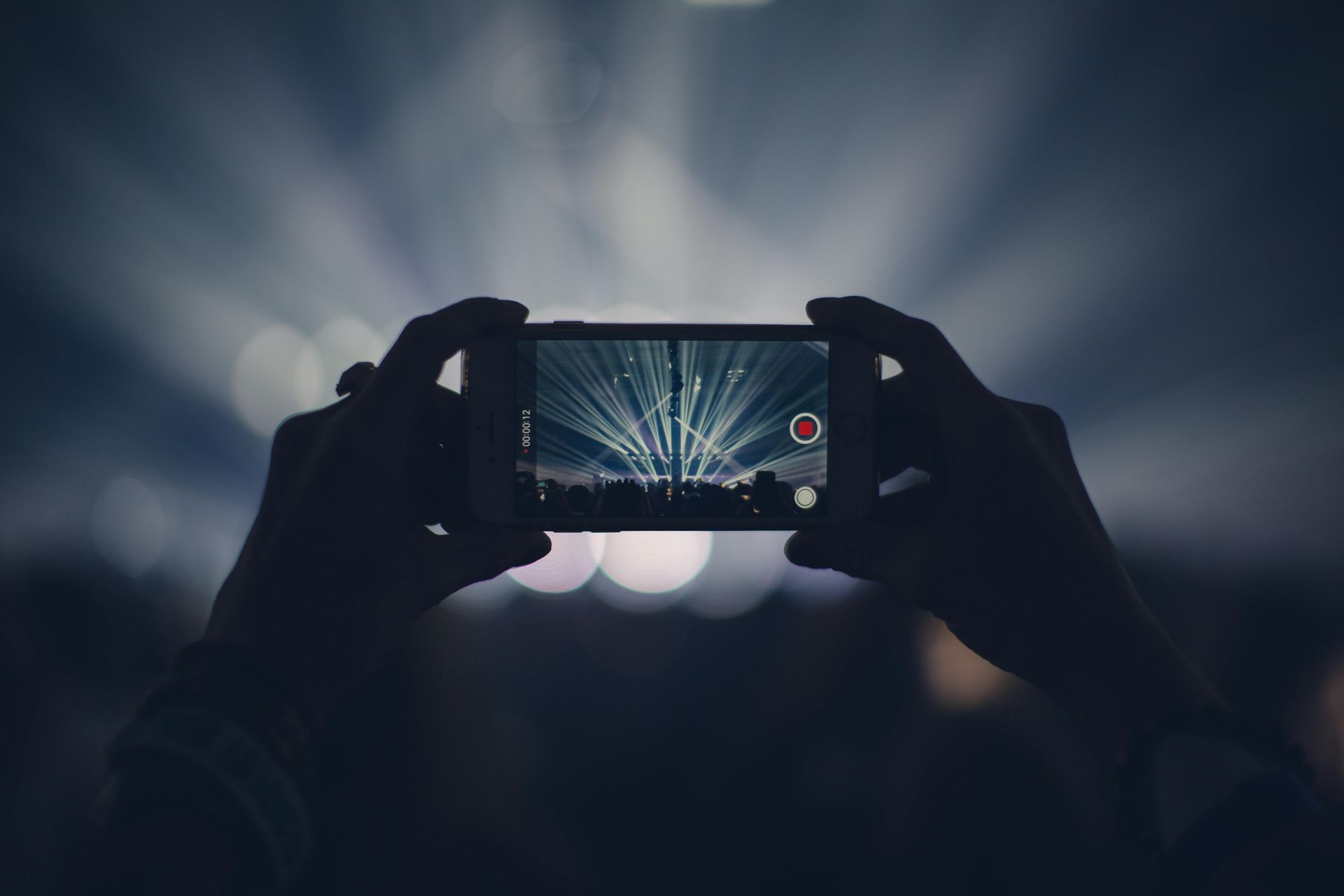 Person recording live concert on phone with bright lights
