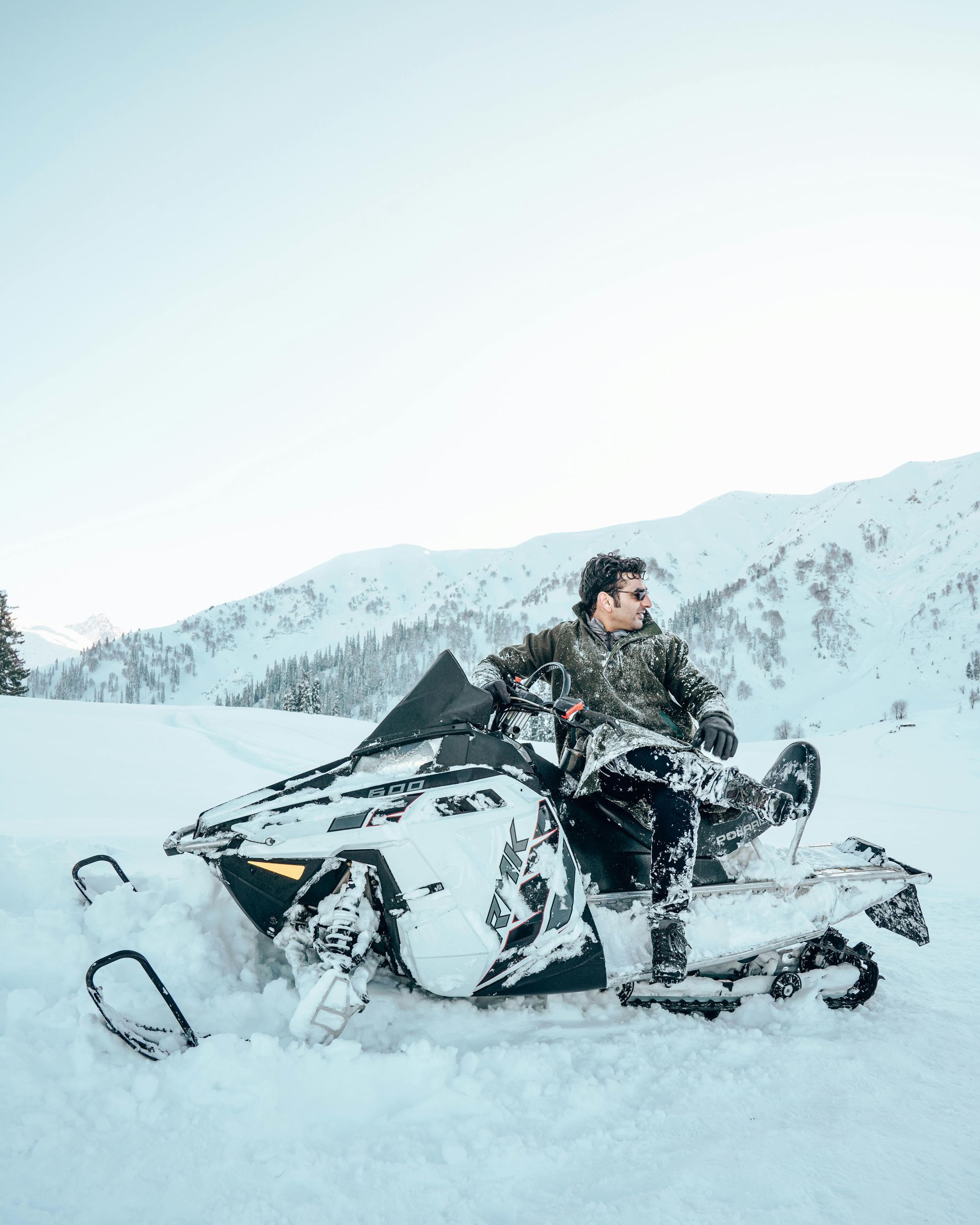 Man covered in snow sitting on snowmobile in warm clothes