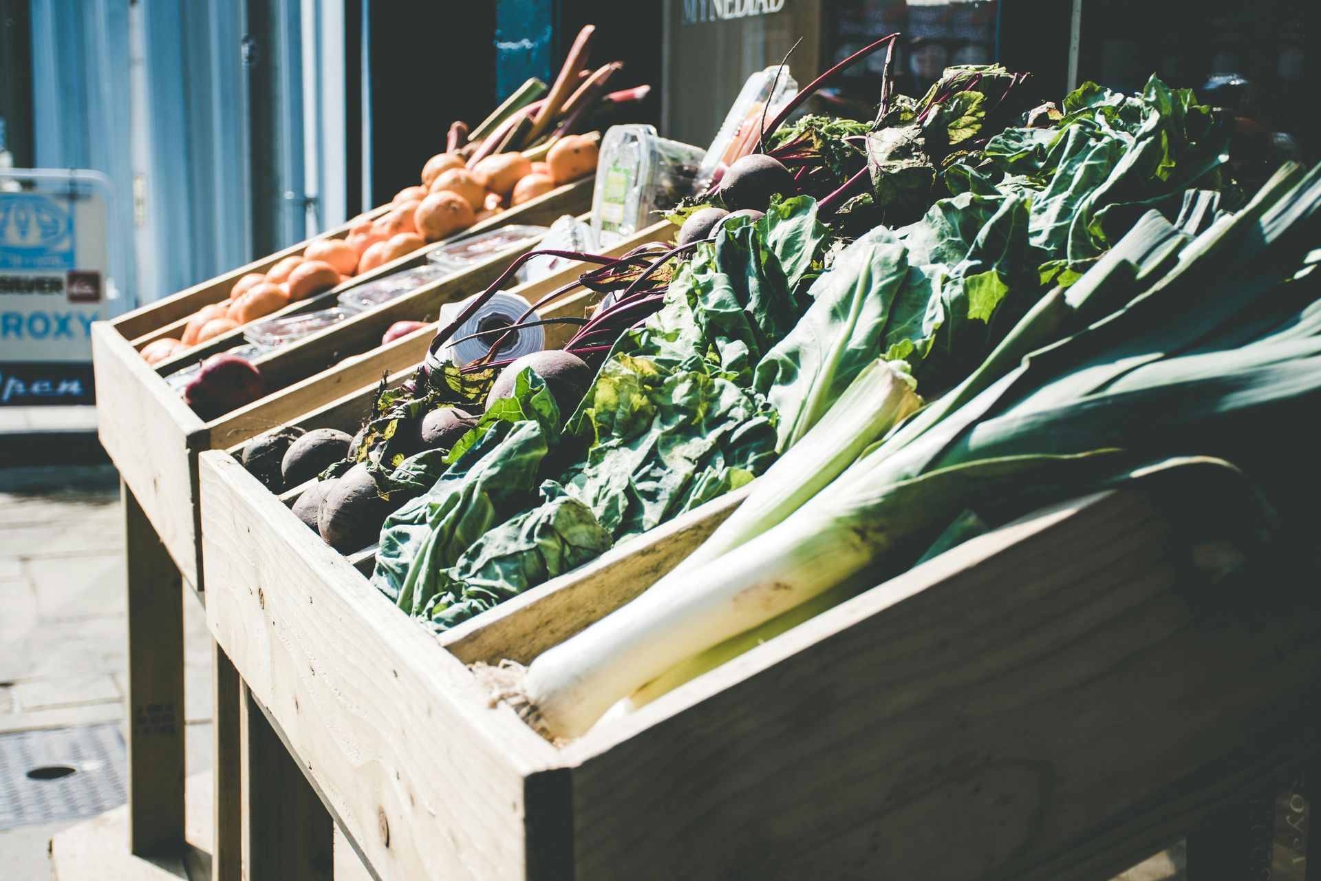 Fresh vegetables sitting outdoors in wooden boxes for purchase at a farmer's market