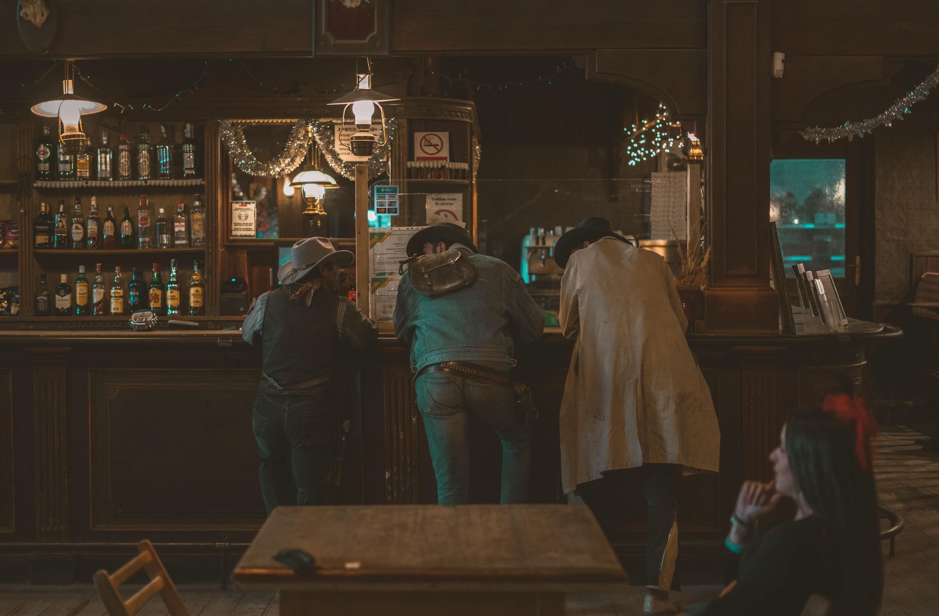 Three cowboys leaning against a bar with drinks and live music in sight