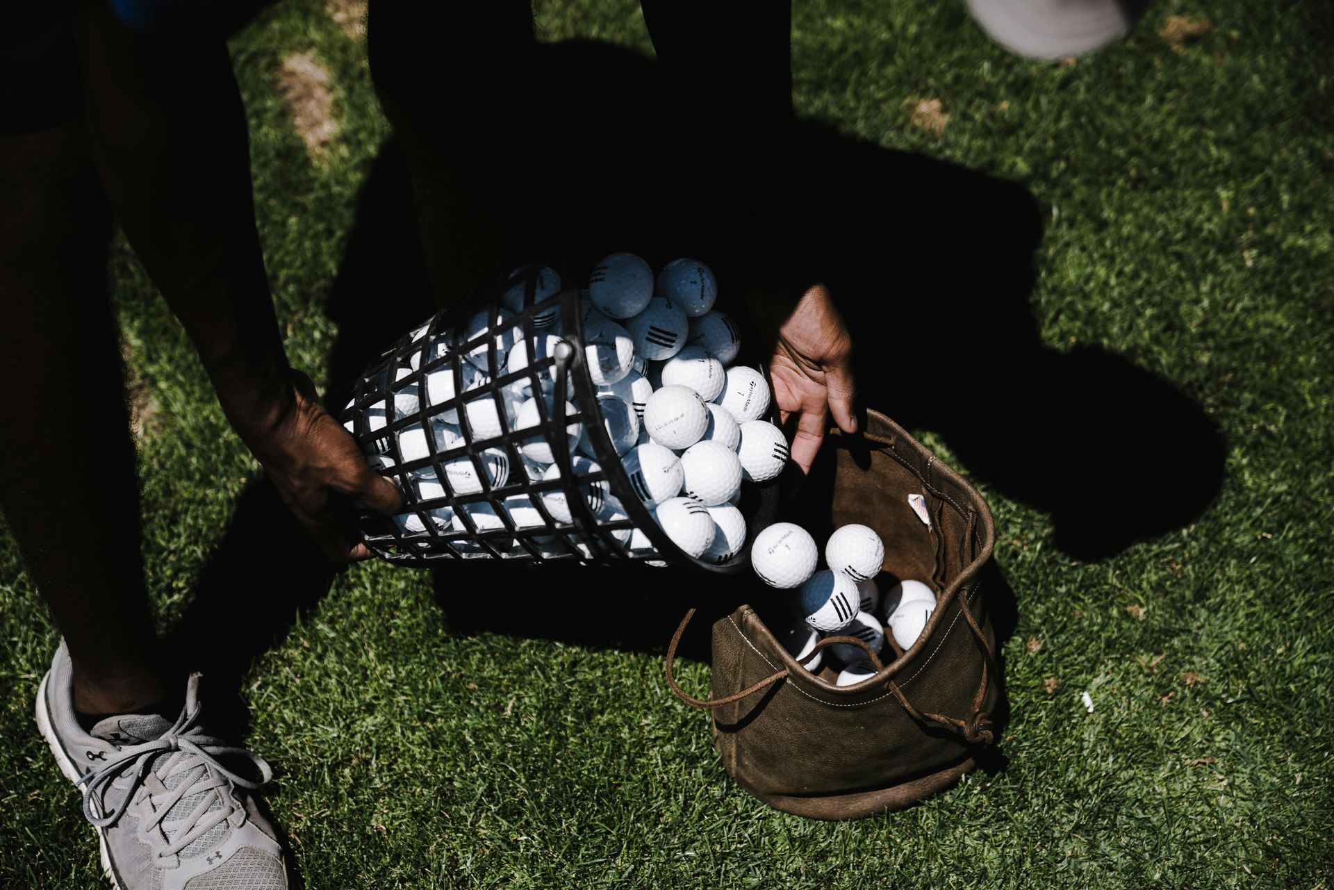 Person pouring several golf balls from bucket into a golf bag on the green
