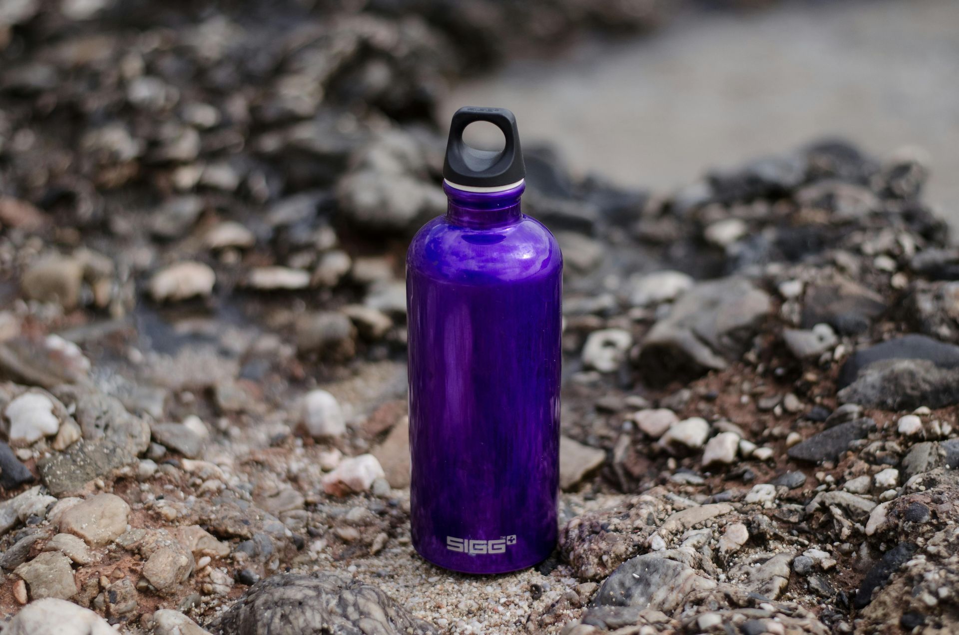 Water bottle sitting on shoreline rocks with water in the background