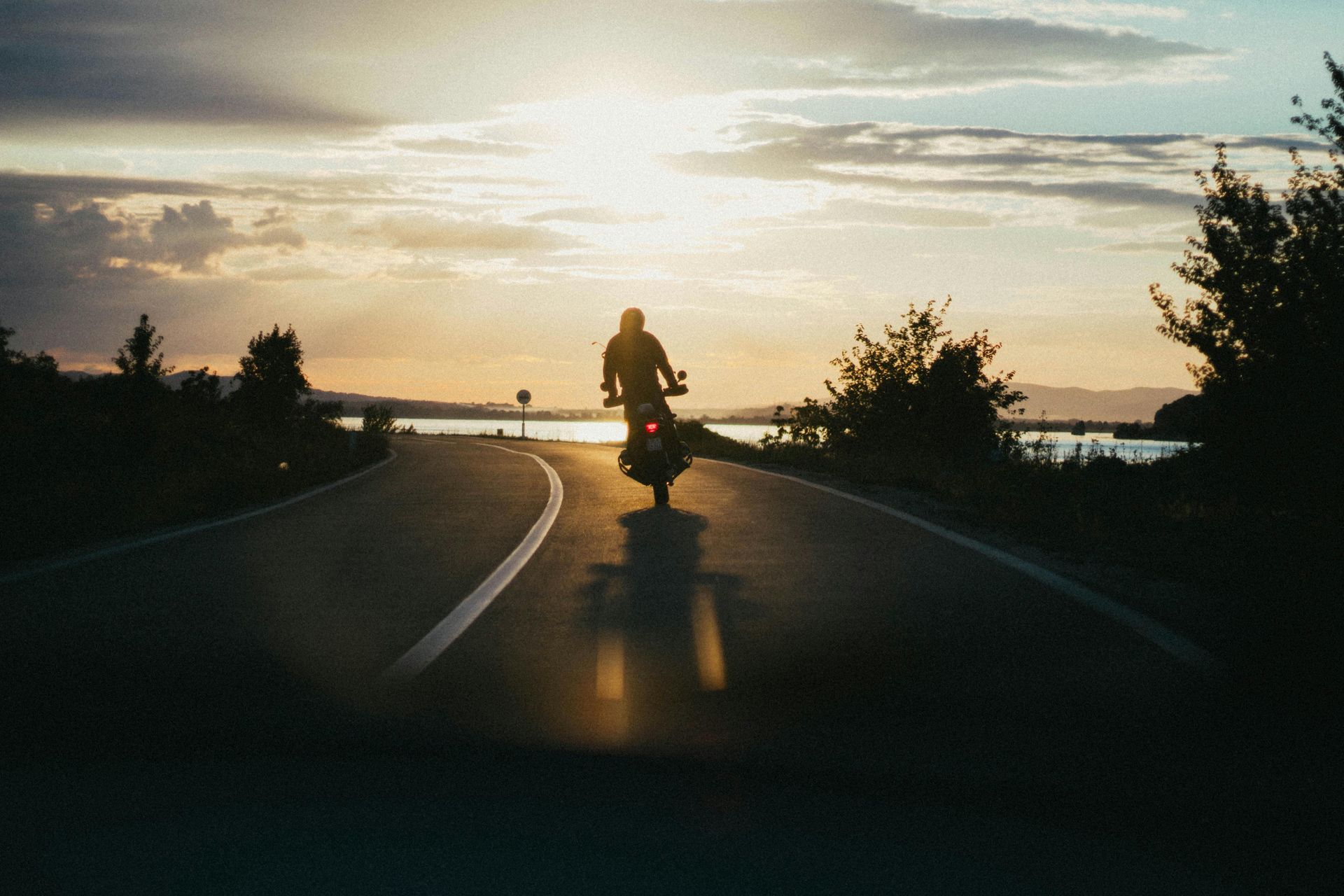 Person riding down a street on motorcycle during sunset
