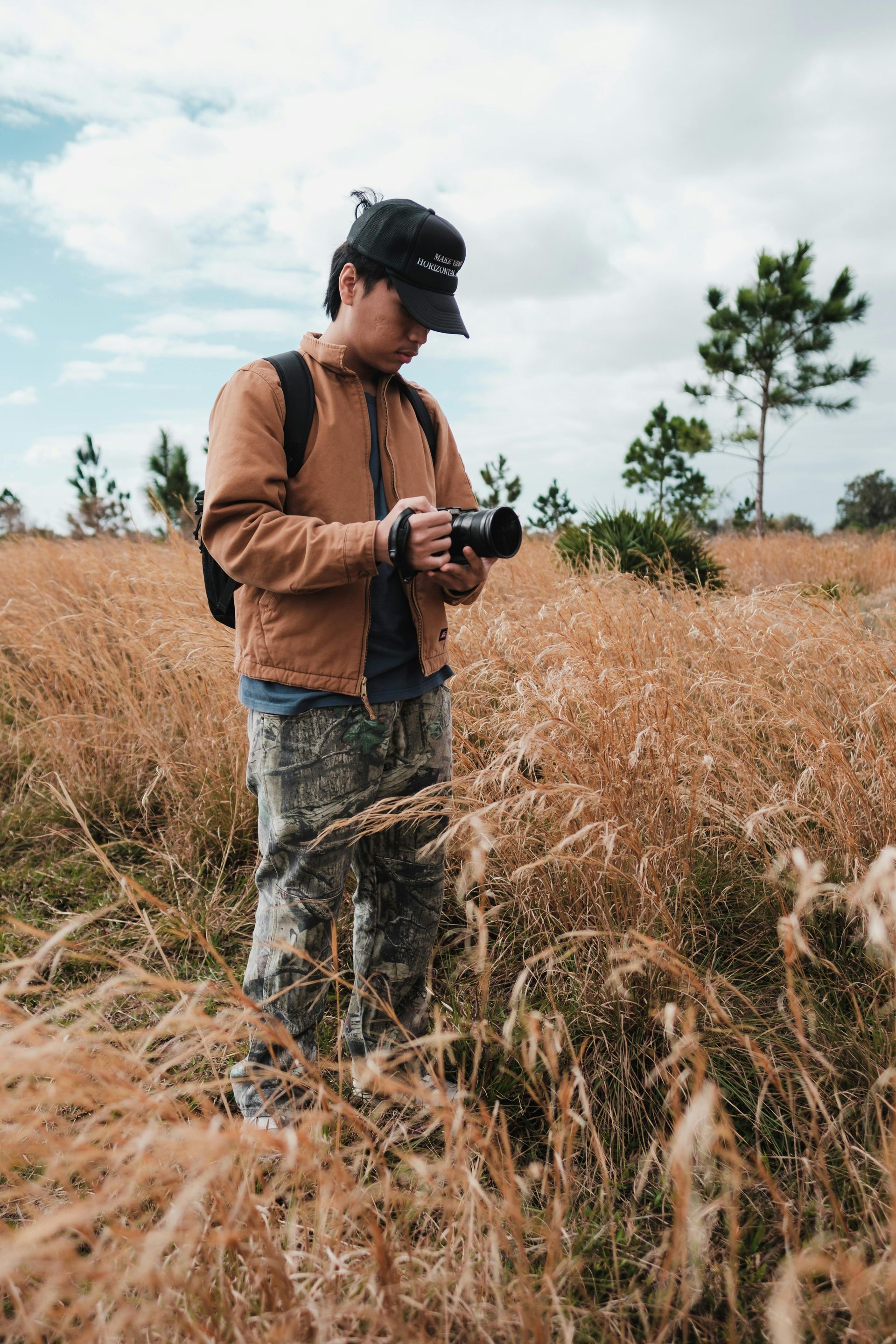 Man standing in tall grass taking pictures with a camera
