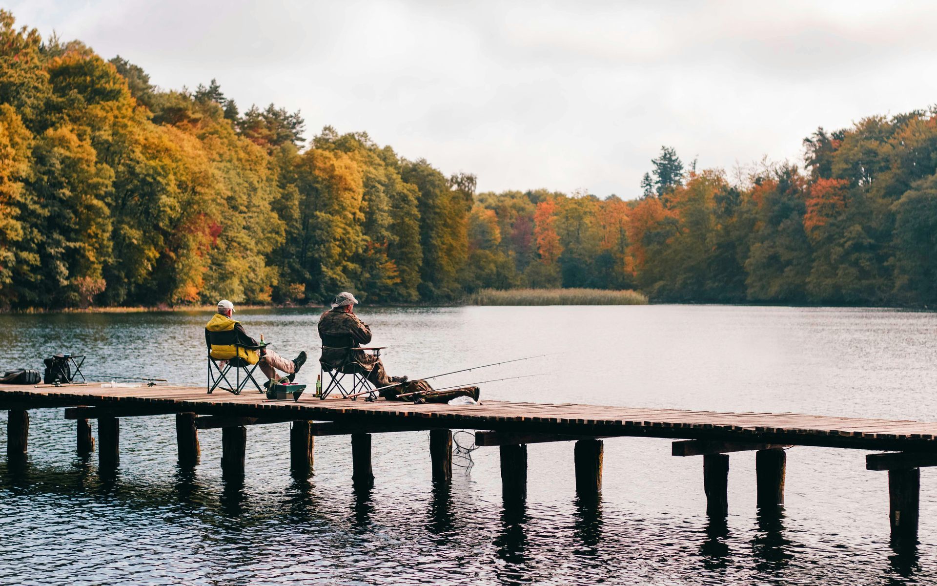 Two people sitting on log dock, fishing in river with beautiful changing color leaves