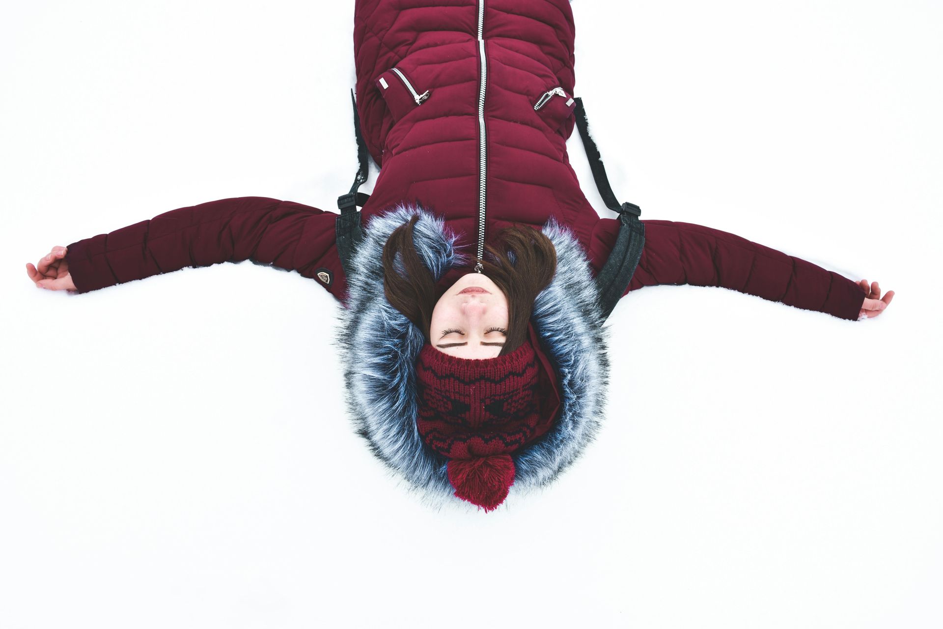 Woman in layered clothing laying in the snow with eyes closed 