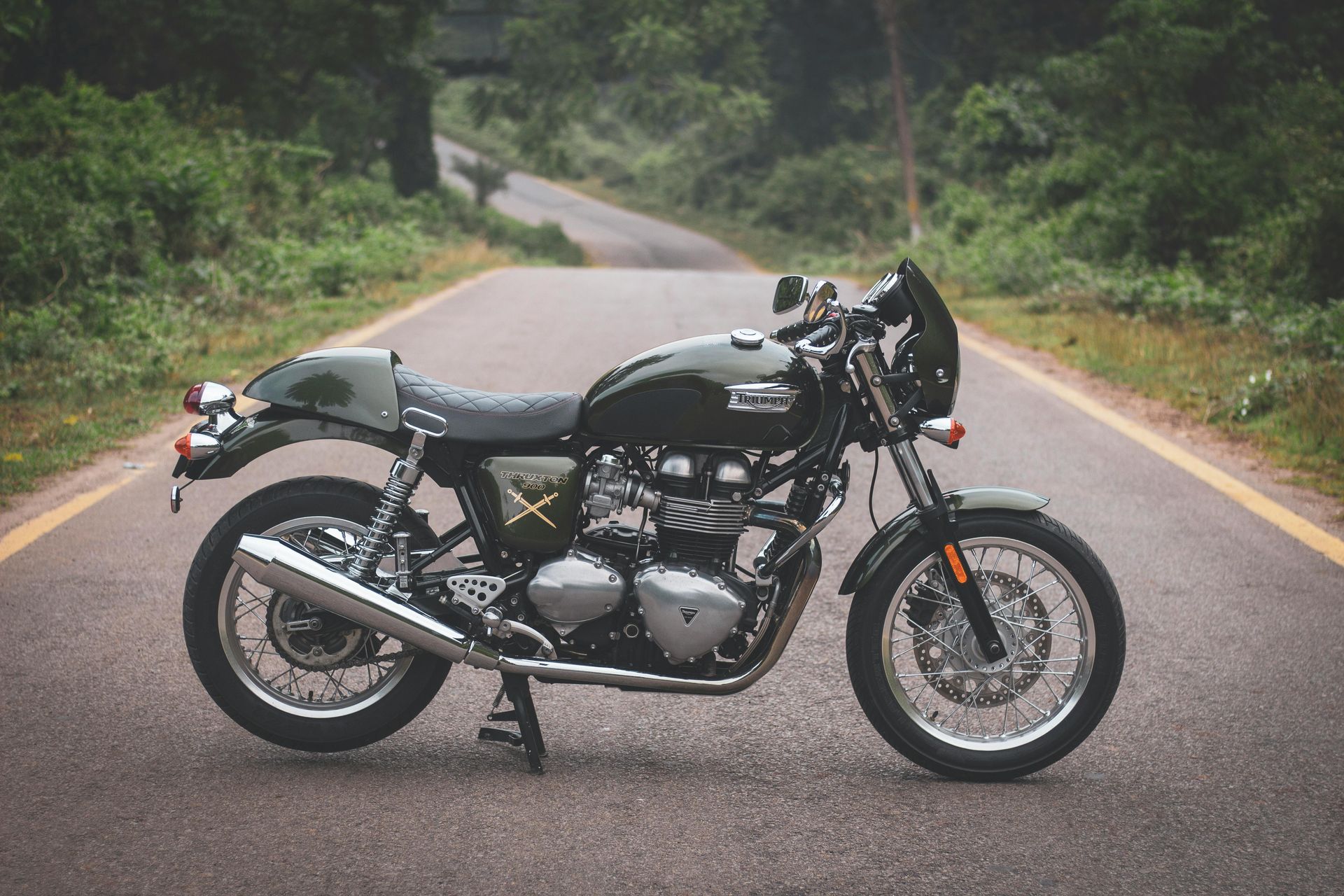 Motorcycle parked in the middle of a road in between bright green trees
