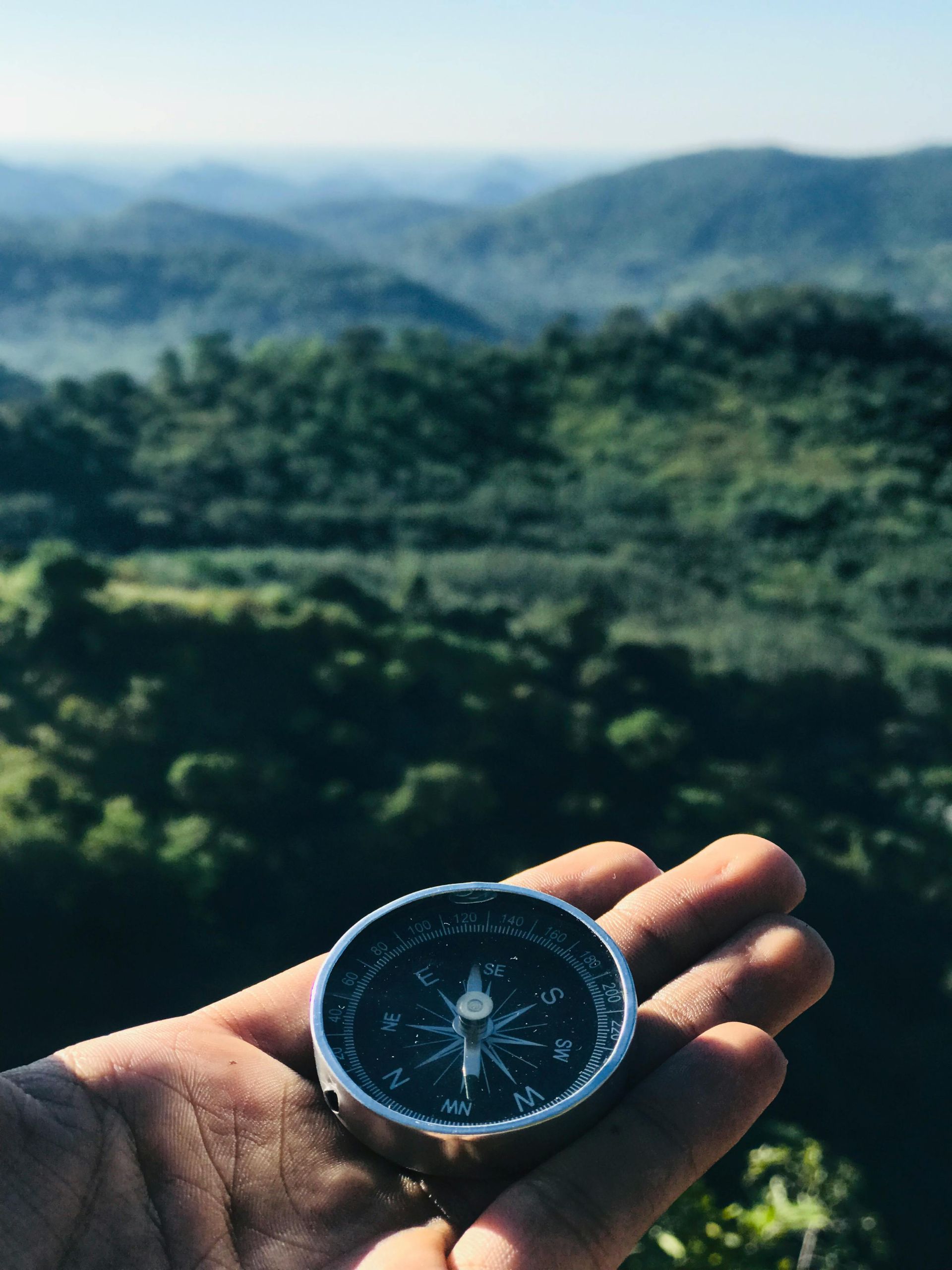 Compass in hand with beautiful hills and lush green trees nearby