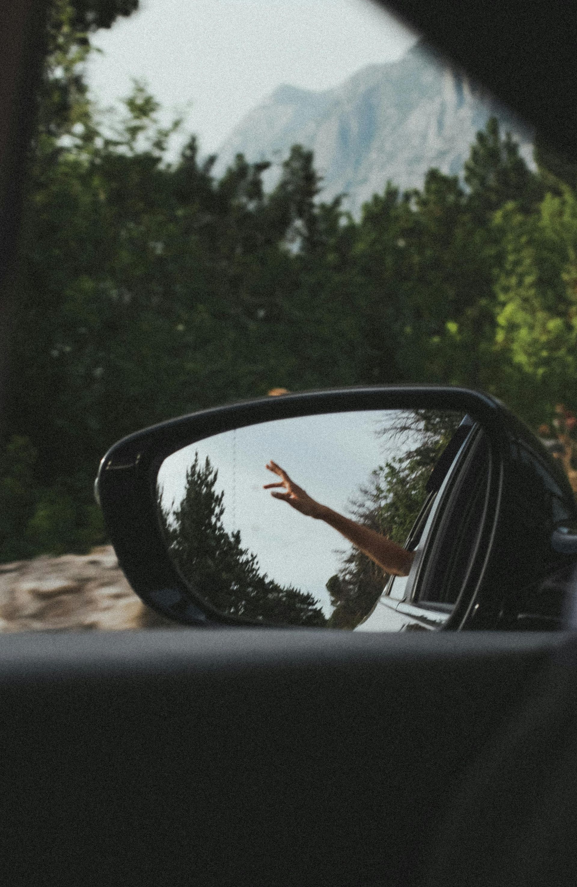 Rearview mirror of a car traveling down the road with a person's hand outside the window