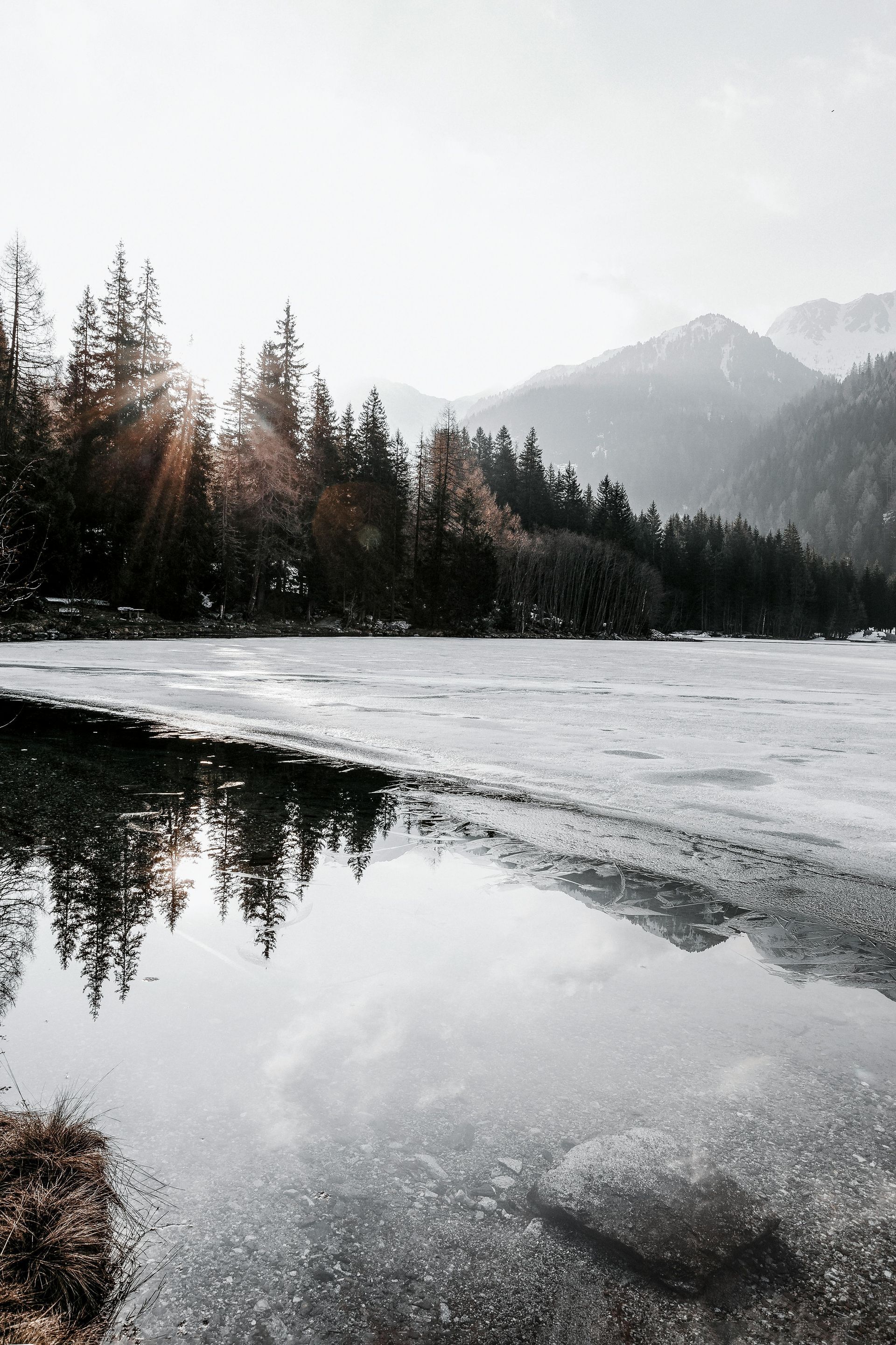 Sunlight over a partially frozen lake reflects in the quiet winter wilderness